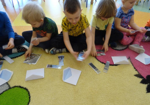 Czwórka dzieci siedzi na dywanie, każde dziecko układa obrazek z części przedstawiający dinozaura.